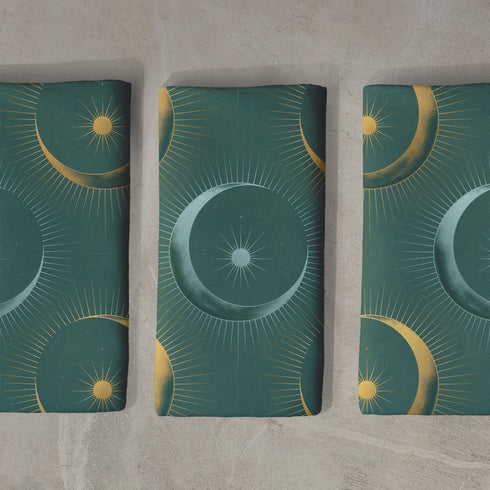 Four-piece cloth napkin set featuring a celestial print of radiant golden crescent moons and pale sunburst orbs against a rich emerald green background. Each napkin displays symmetrical, glowing motifs inspired by lunar phases and cosmic geometry. The fabric is neatly folded to showcase the repeating pattern, with a soft matte finish and fine detailing, perfect for mystical or magical table settings, altar decor, or celestial-inspired dining aesthetics.